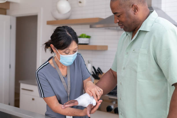 A female doctor of Asian descent makes a house call. The patient is a mature black man with an injured wrist. Occupational therapy, physical therapy, and home health concepts.